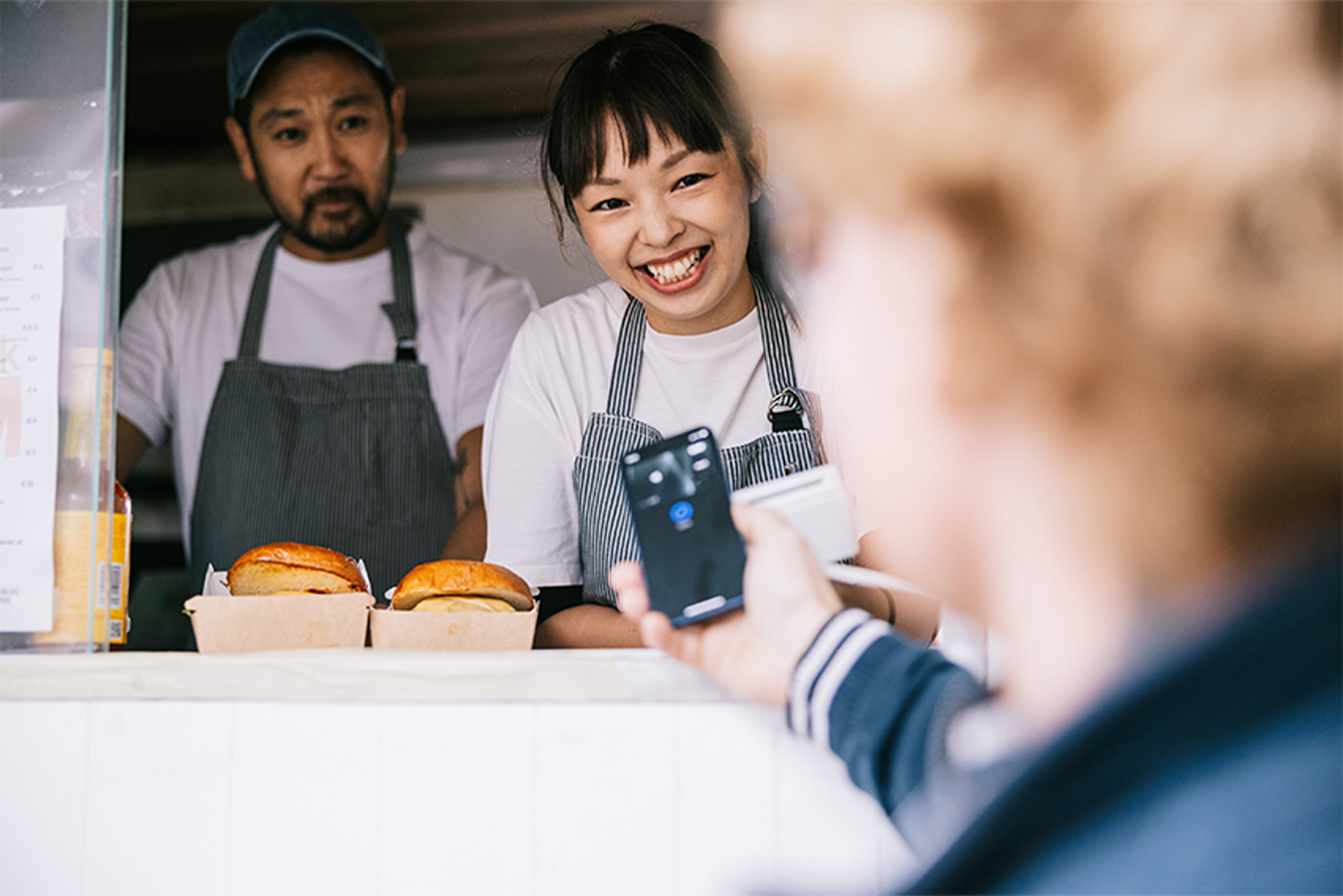 Food truck employees smiling to a customer who is paying for food with a cell phone.