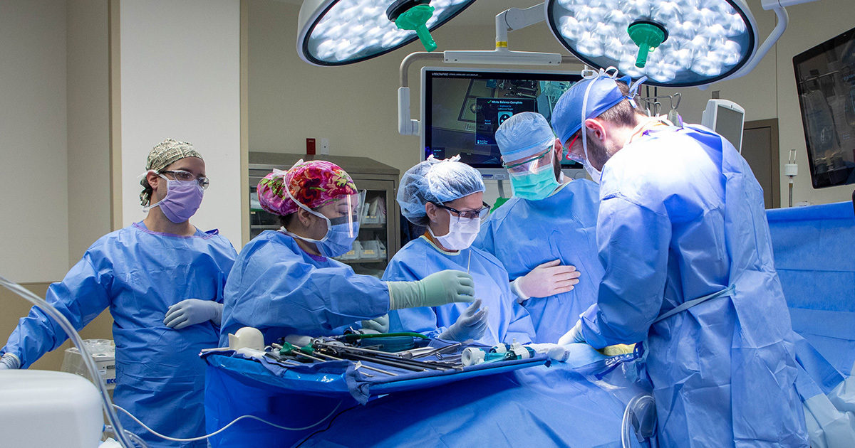 Dr. Turgeon, Dr. Adler, and three other care team members in blue full scrubs gather around kidney donor Victorai Threadgould in the OR.