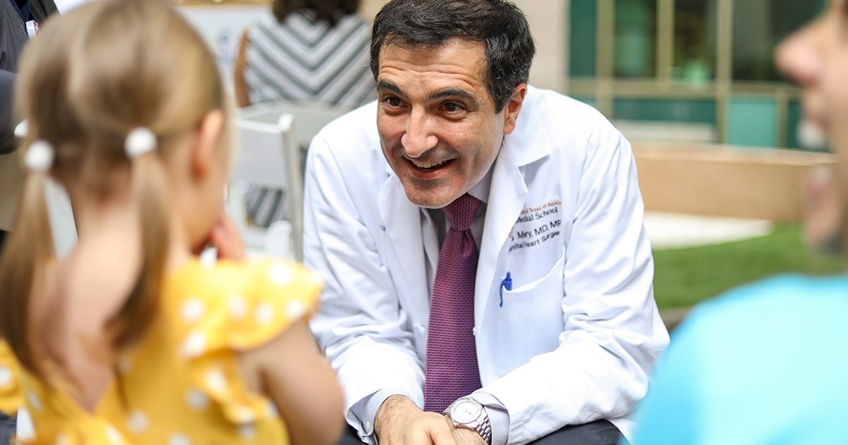 Dr. Carlos Mery smiles at a young girl. Her back is turned to the camera.