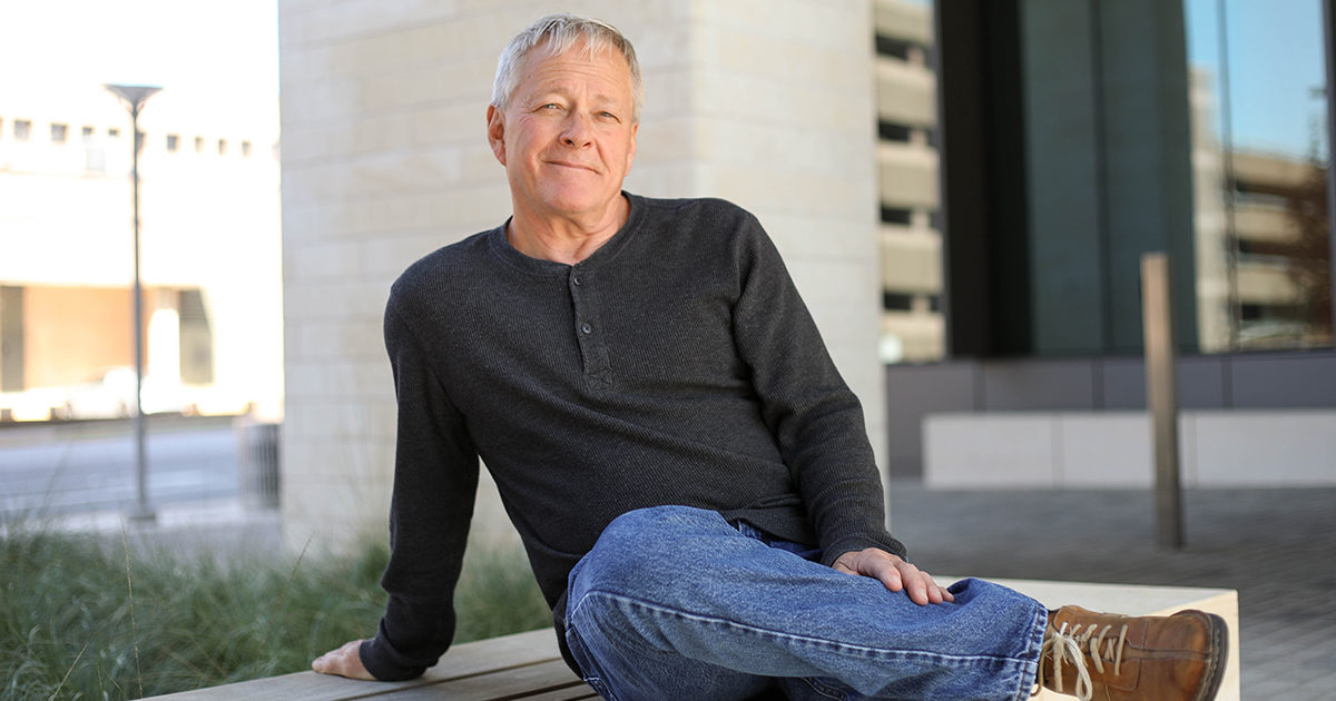 John, a patient with the Musculoskeletal Institute, sits on an outdoor bench, smiling at the camera.