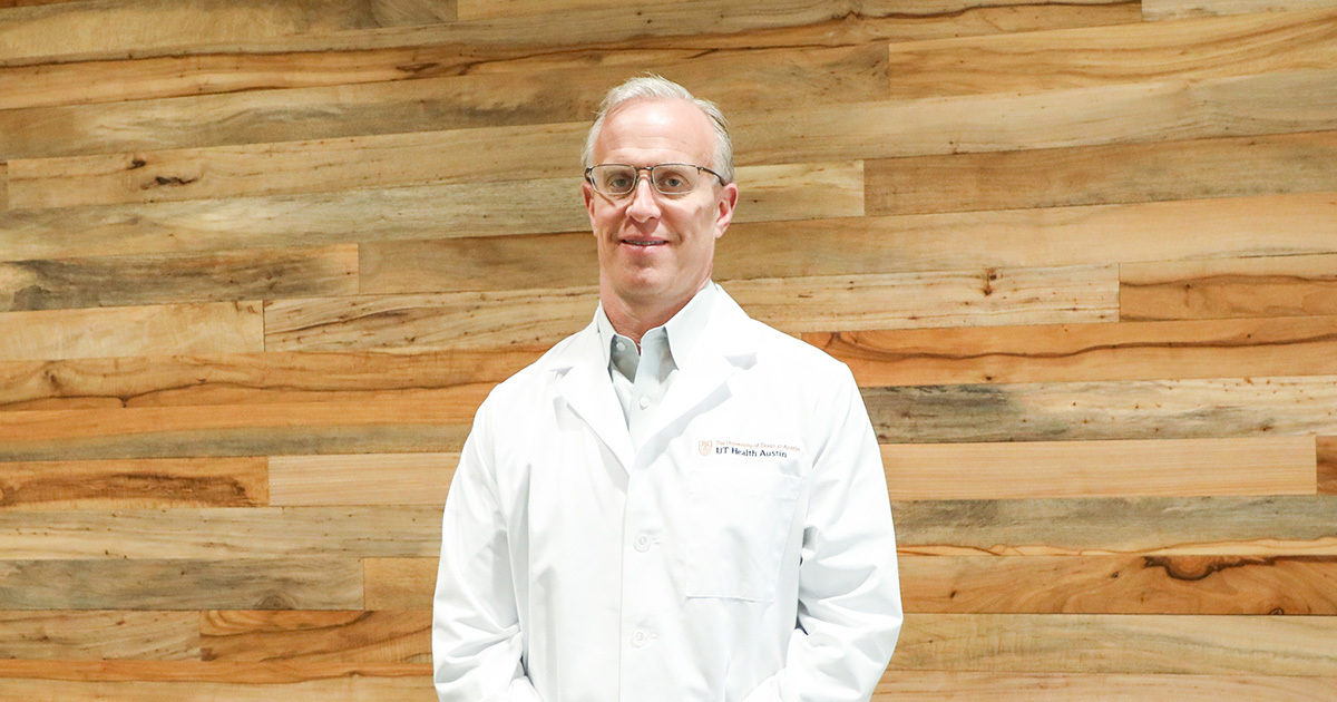 Kevin Bozic, MD, MBA, FAOA, FAAOS Executive Director, Musculoskeletal Institute, stands smiling in front of a wood-paneled wall. His hands are folded.