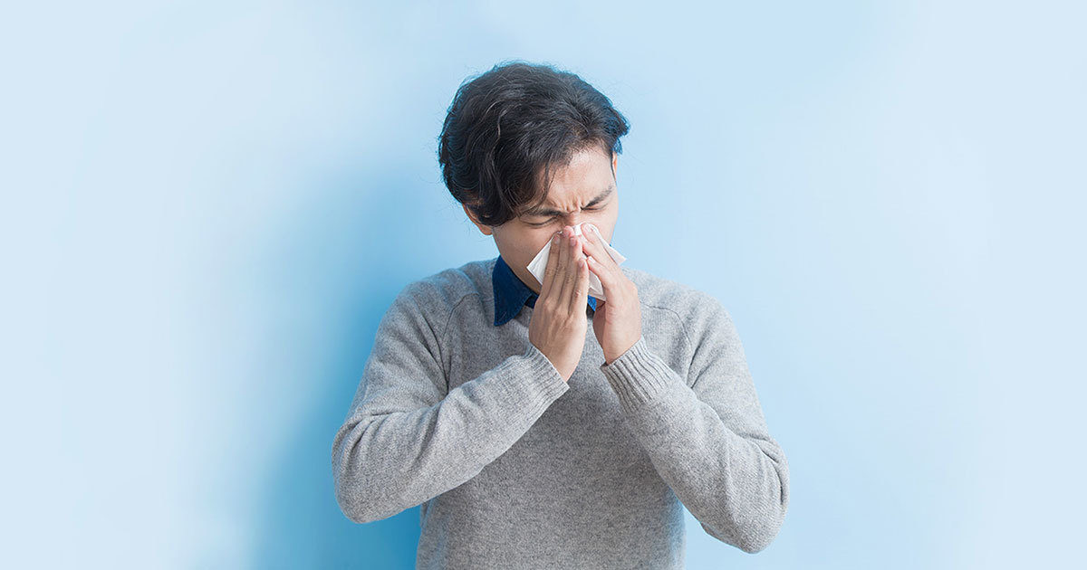 A man is seen sneezing into a tissue held between his hands.