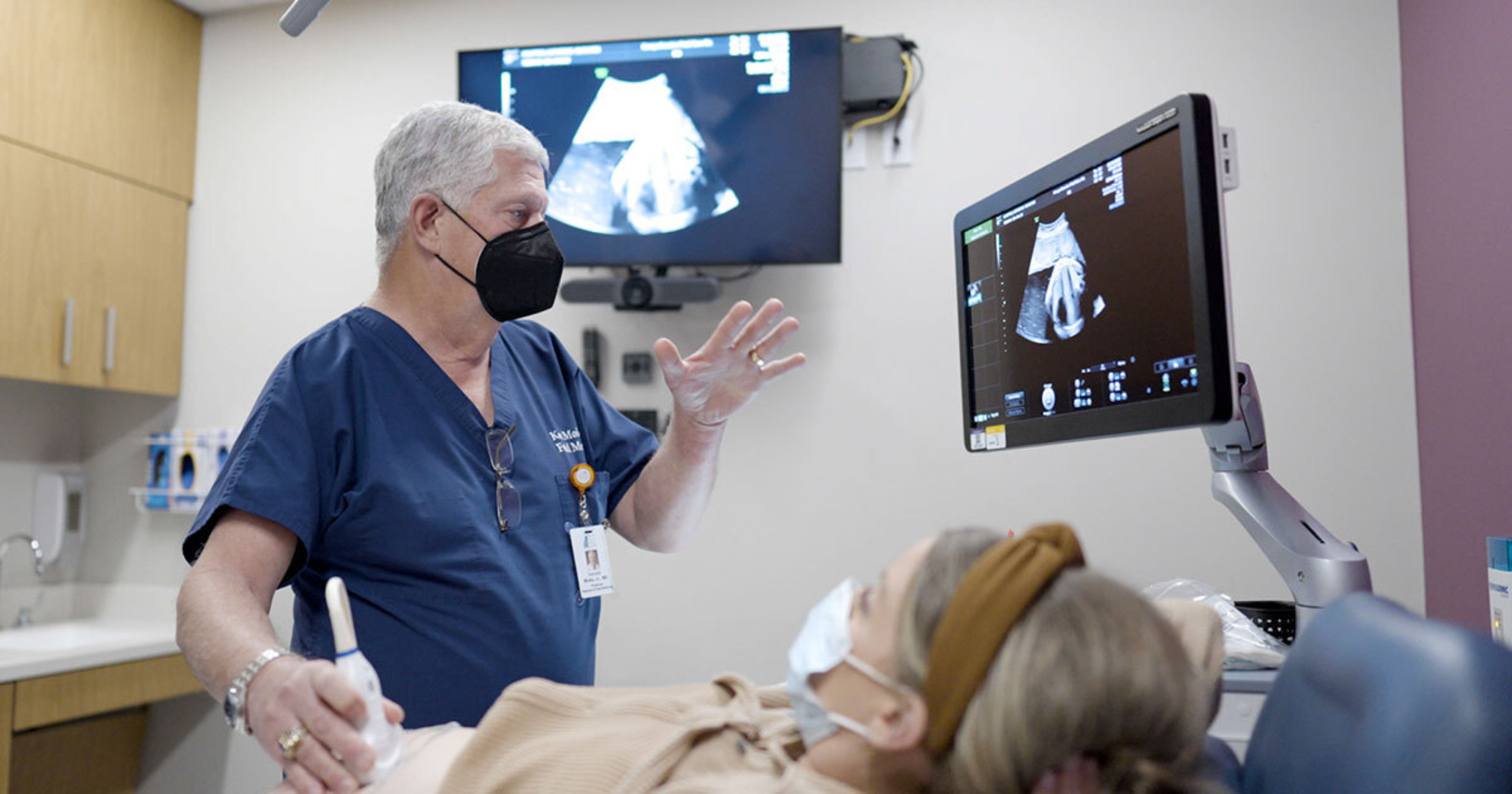 Dr. Kenneth J. Moise, Jr., performing a fetal ultrasound on a woman in a brown shirt. Both he and the patient are wearing masks.