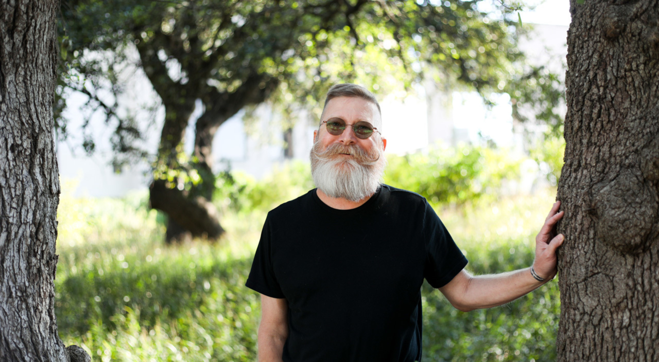 David Warren stands outside with his hand resting on a tree.