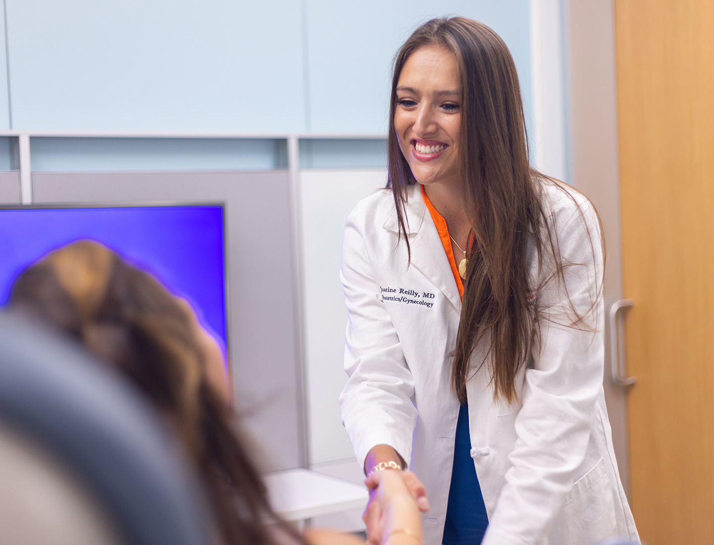 Justine Reilly, MD, an ob-gyn in Women's Health, wearing a white coat and shaking the hand of a patient whose back is to the camera.