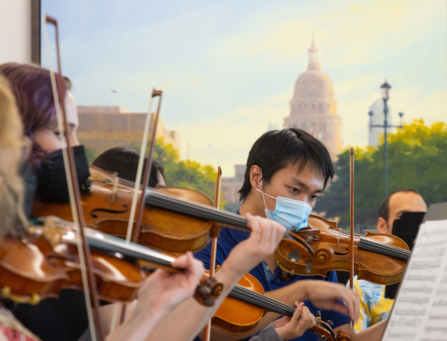 A masked string orchestra performing with the Texas State Capitol building in the background.