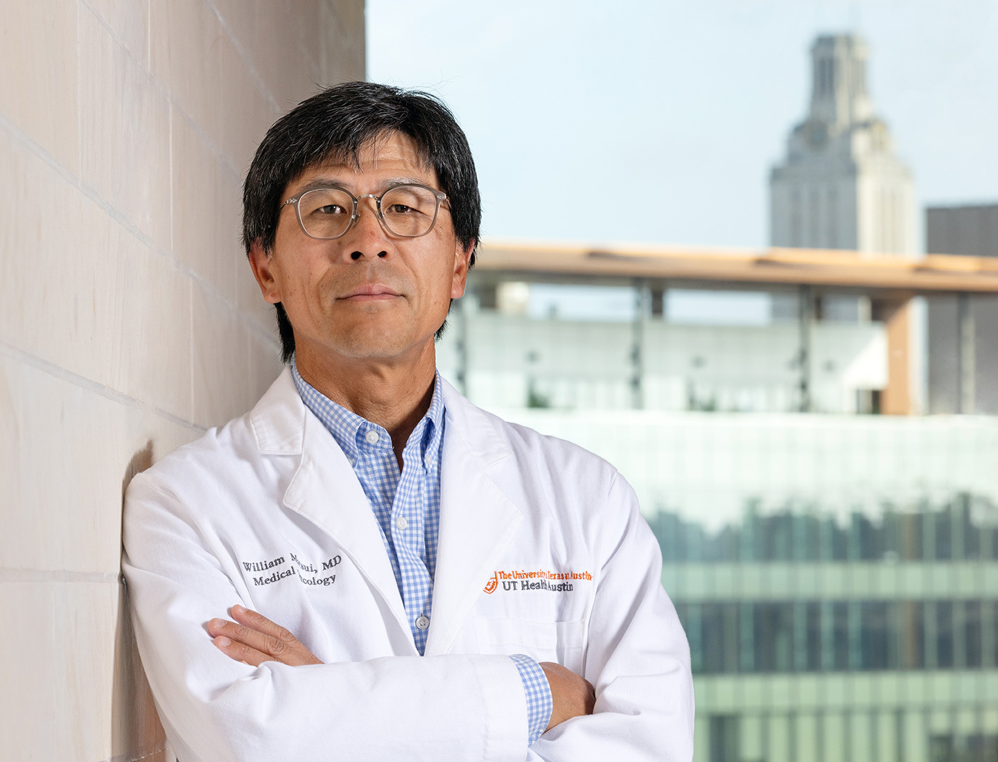 William Matsui, MD, posing in a white lab coat with the UT Tower visible behind him.