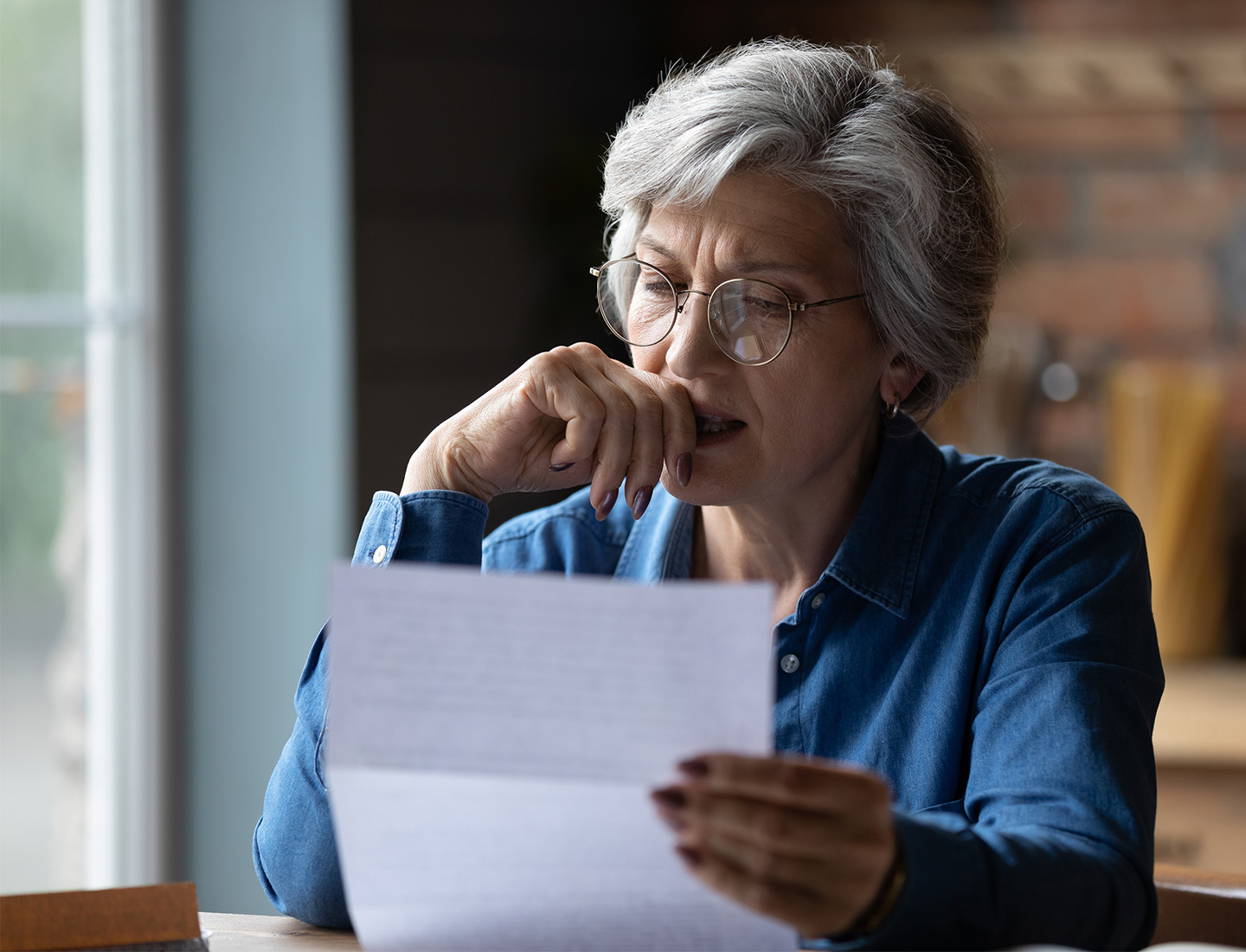 A gray-haired woman with glasses looking intently at a sheet of paper in her hands