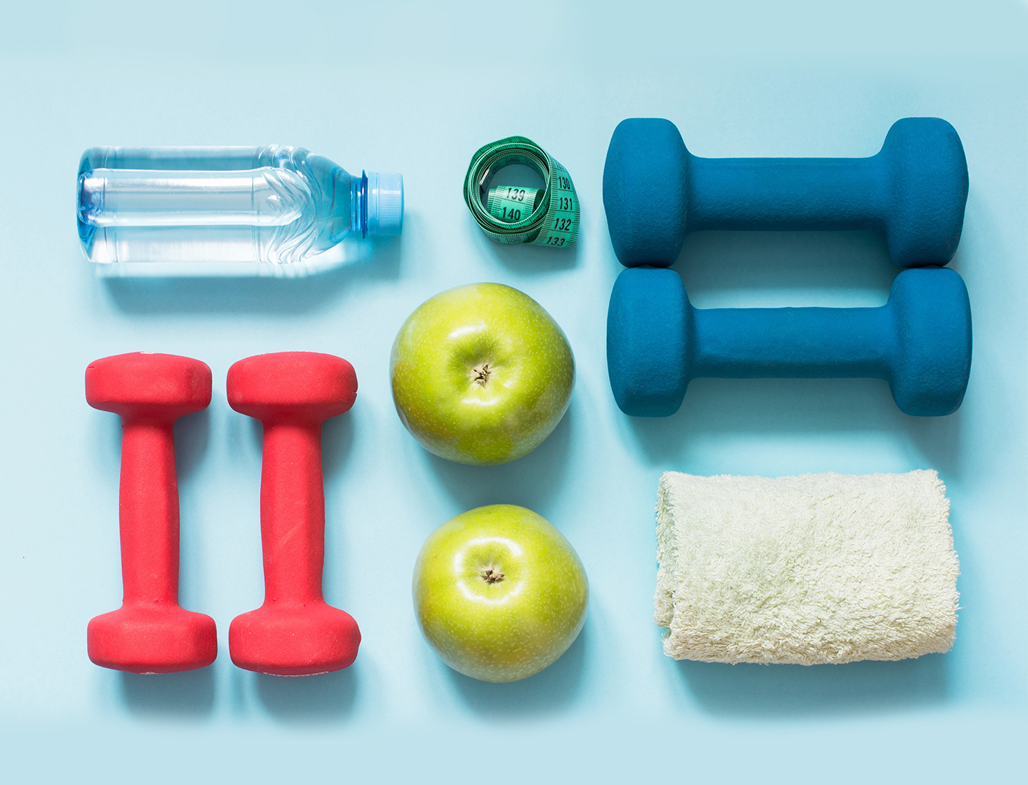 A water bottle, tape measure, two sets of weights, two apples, and a towel pictured on a blue background.