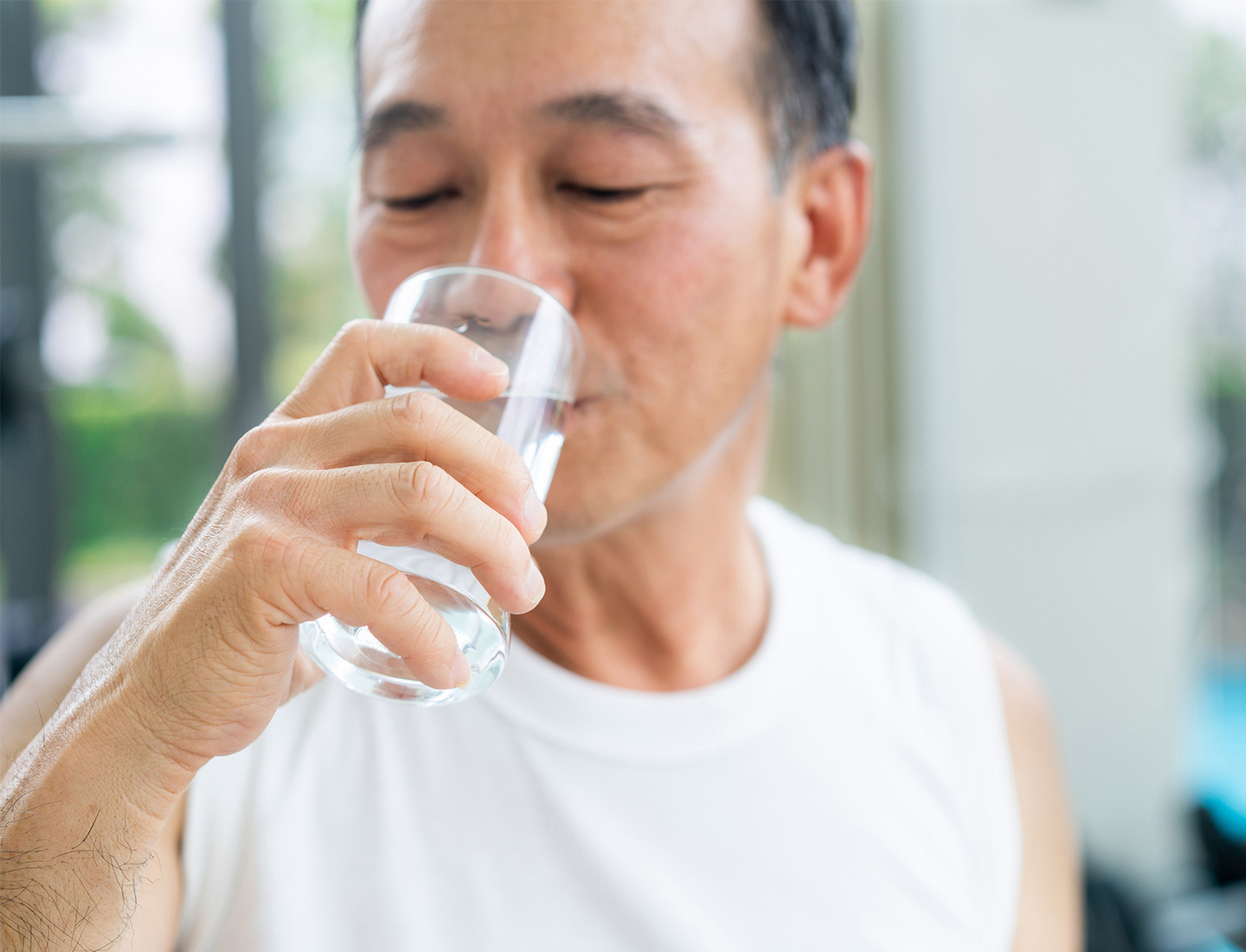 A middle-aged Asian man drinking a glass of water.