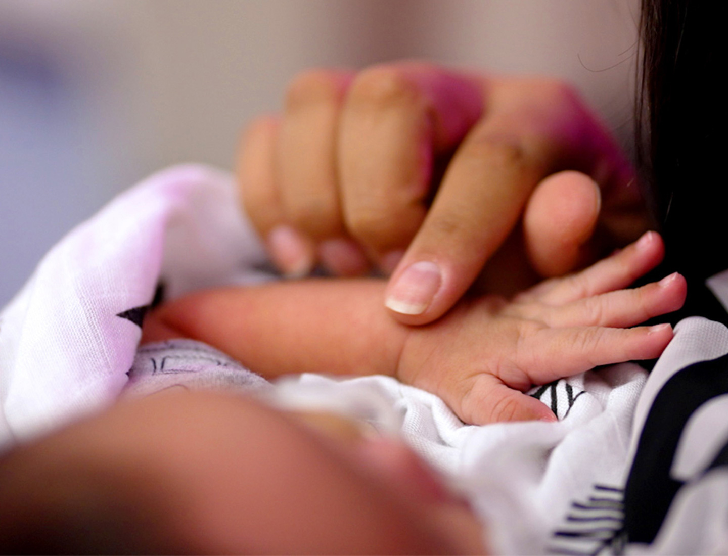 A closeup of a woman's hand stroking the top of a swaddled baby's wrist.