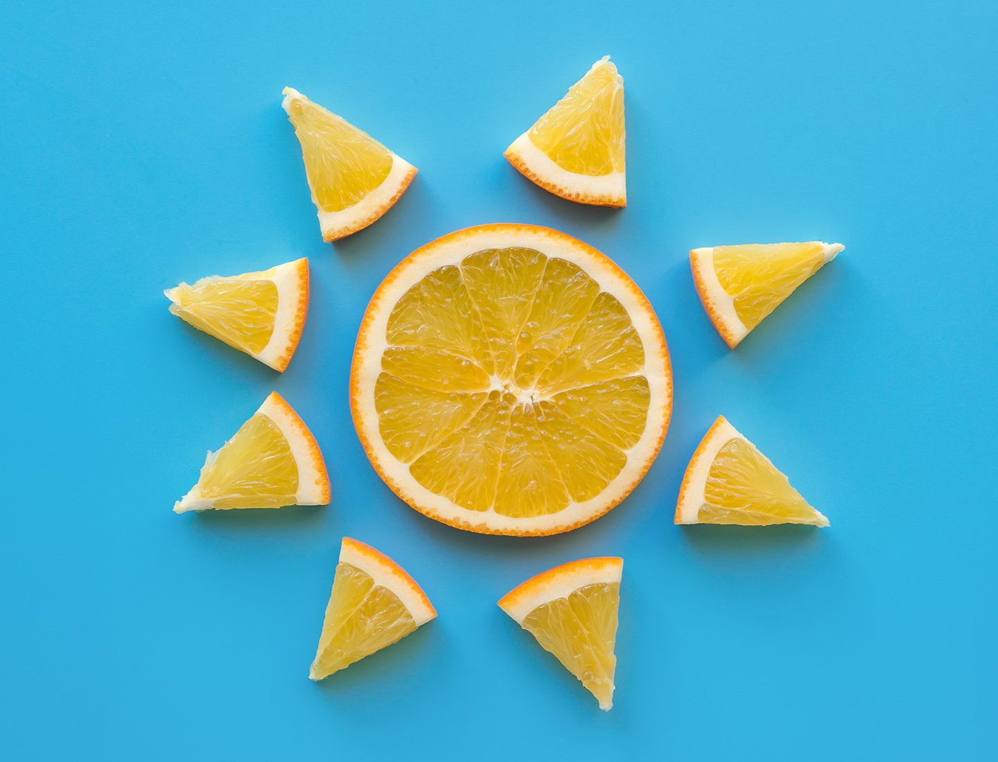 Orange slices are arranged in the shape of a sun on a light blue surface.