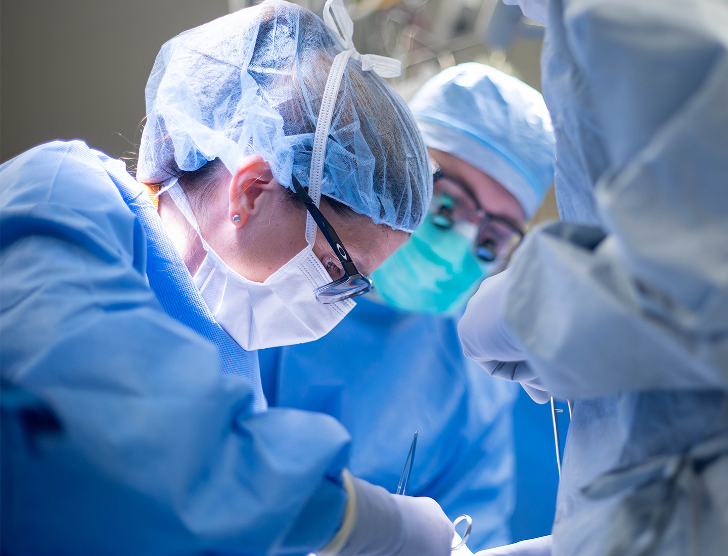 Dr. Nicole Turgeon performing a procedure in the operating room as another team member looks on. Both are wearing surgical masks, head coverings, gloves, and gowns.