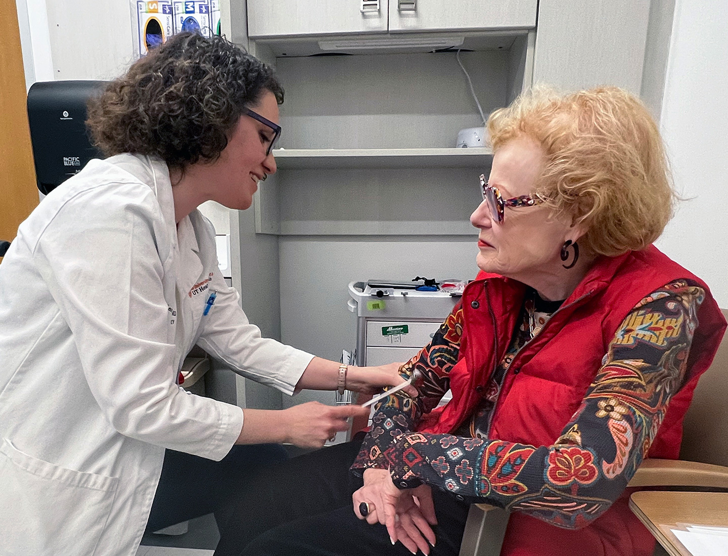 Leoráh Freeman, MD, PhD, performing a reflex test on Vicki Almond in an exam room.