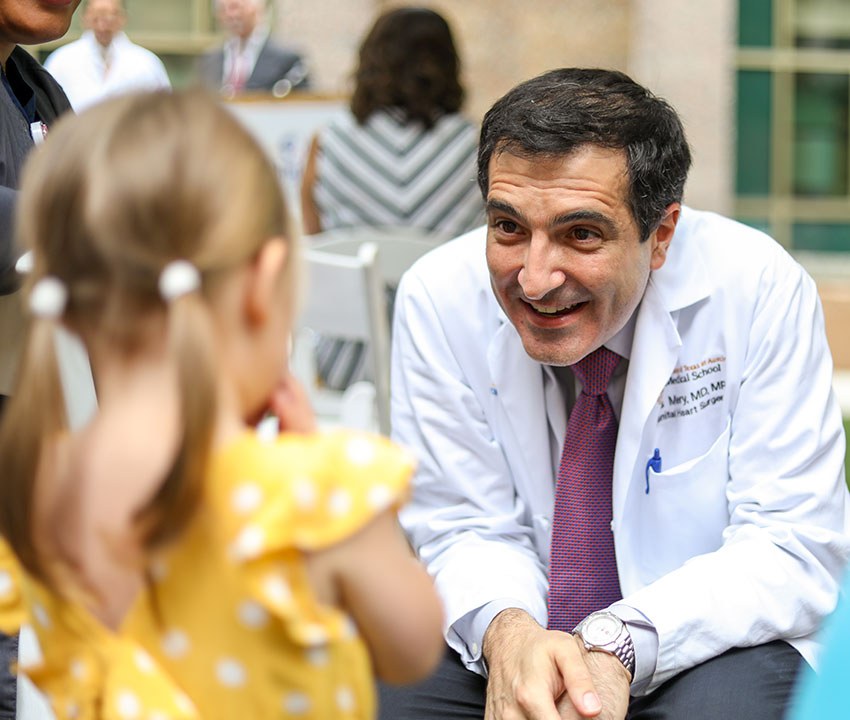 Dr. Carlos Mery smiles at Addy. HEr back is turned to the camera. She wears a yellow dress with white polka dots.