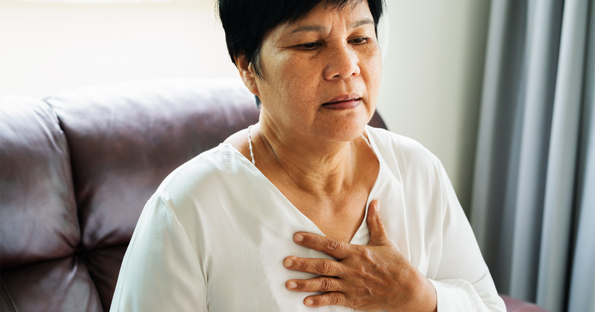 A seated Latin-X woman experiencing heartburn holds her hand to her chest.