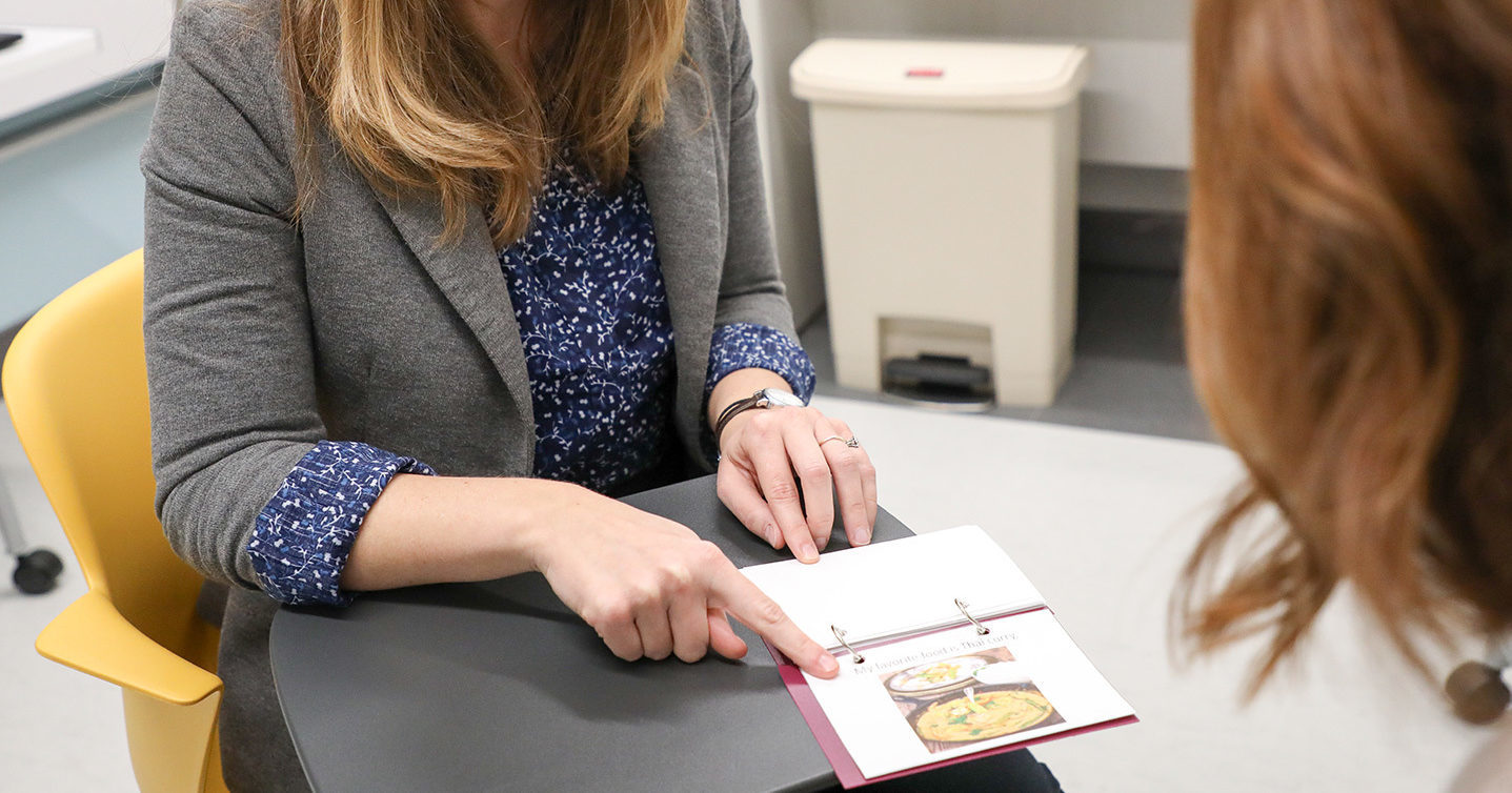 A clinician at UT Health Austin's Comprehensive Memory Center smiles while pointing to a page in a memory book.