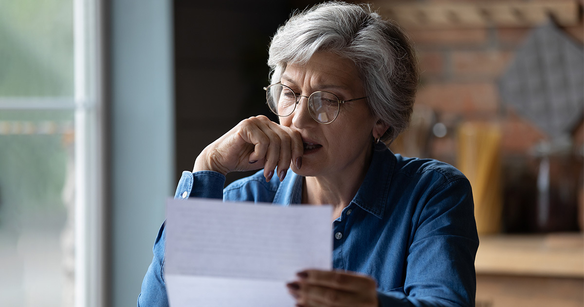A gray-haired woman with glasses looking intently at a sheet of paper in her hands
