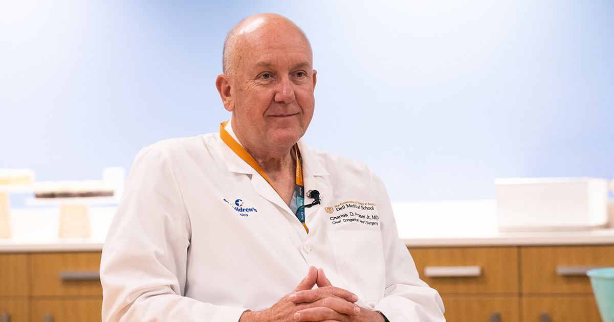 Charles D. Fraser, Jr., MD, wearing a white coat while seated at a table with his hands clasped.