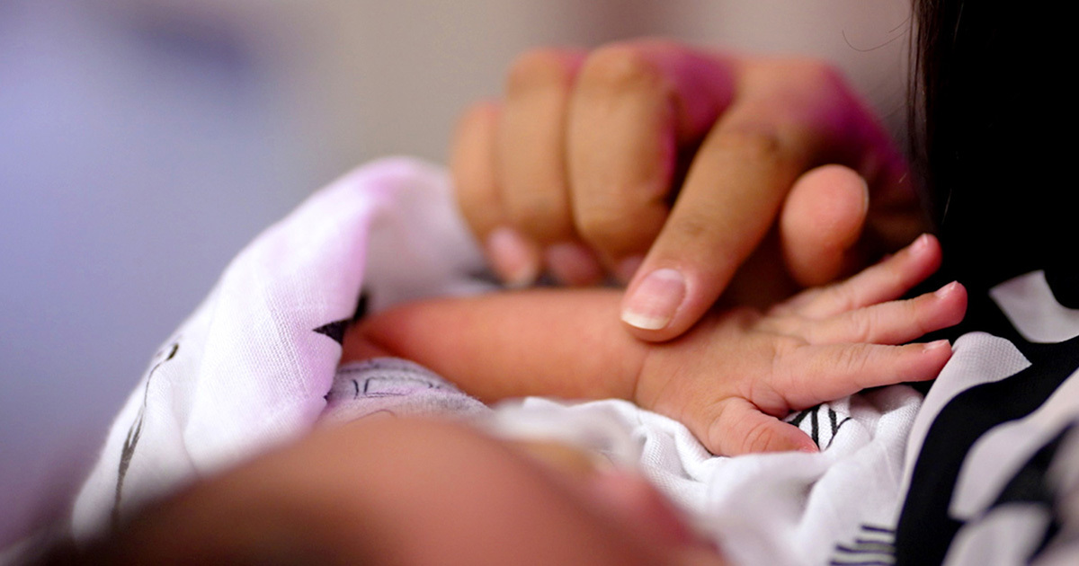 A closeup of a woman's hand stroking the top of a swaddled baby's wrist.