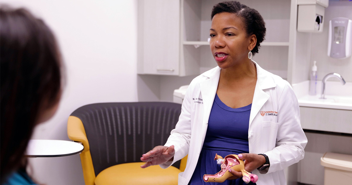 M. Yvette Williams-Brown, MD, holding a model of the female reproductive system in an exam room.