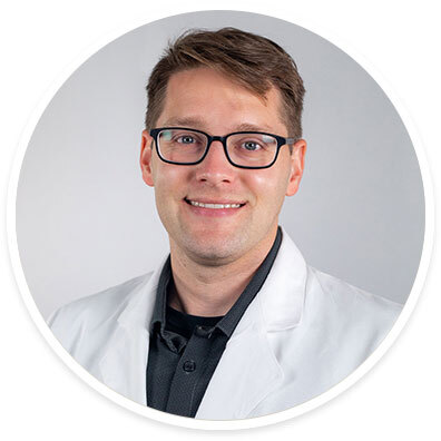 Ophthalmologist Eric Crowell, MD, MPH wearing a white coat and smiling in front of a white backdrop.