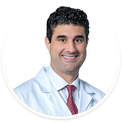 Cardiothoracic surgeon George Arnaoutakis, MD, wearing a white coat and smiling in front of a white backdrop.