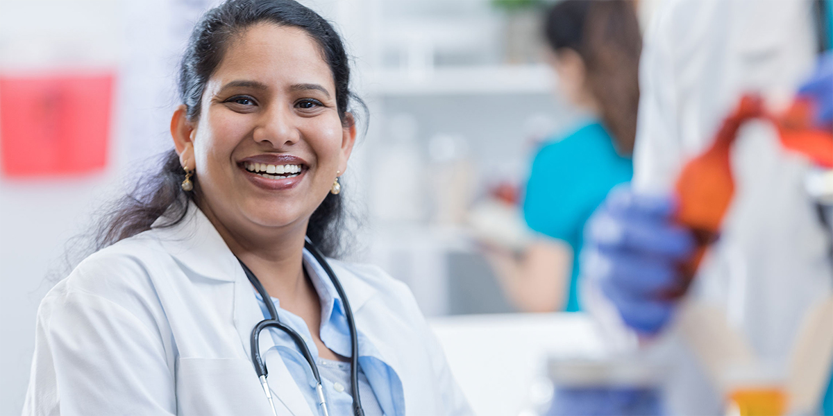 A Latinx female clinician smiles at the camera.