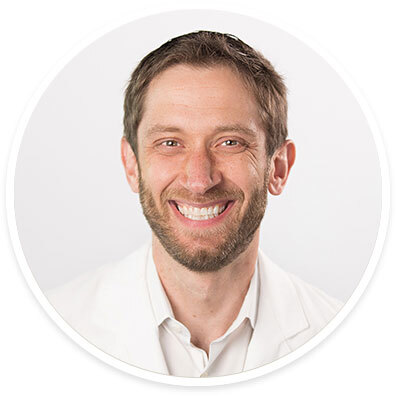 Abdominal transplant surgeon Joel T. Adler, MD, MPH wearing a white coat and smiling in front of a white backdrop.