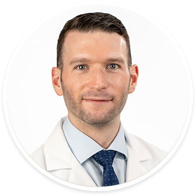 Cardiothoracic surgeon Joshua Grimm, MD, wearing a white coat and smiling in front of a white backdrop.