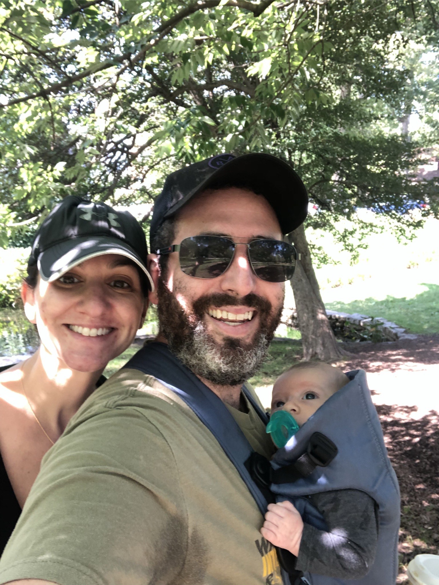 Julia, her husband, and their child pose for a selfie outdoors.