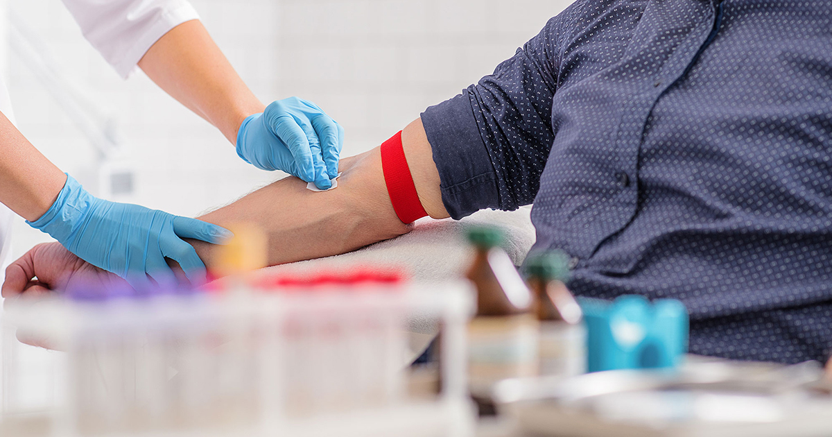 Close up of someone wearing gloves swabbing a patient's arm with an alcohol pad.