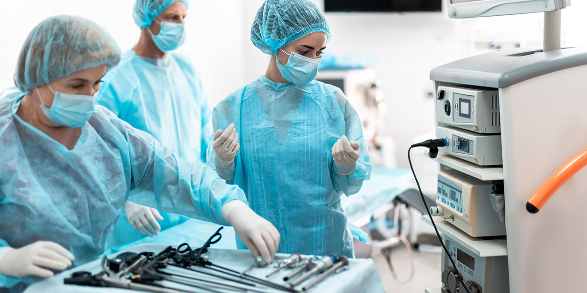 Providers in the operating room wearing gowns, masks, gloves, and head coverings near a tray of surgical equipment.