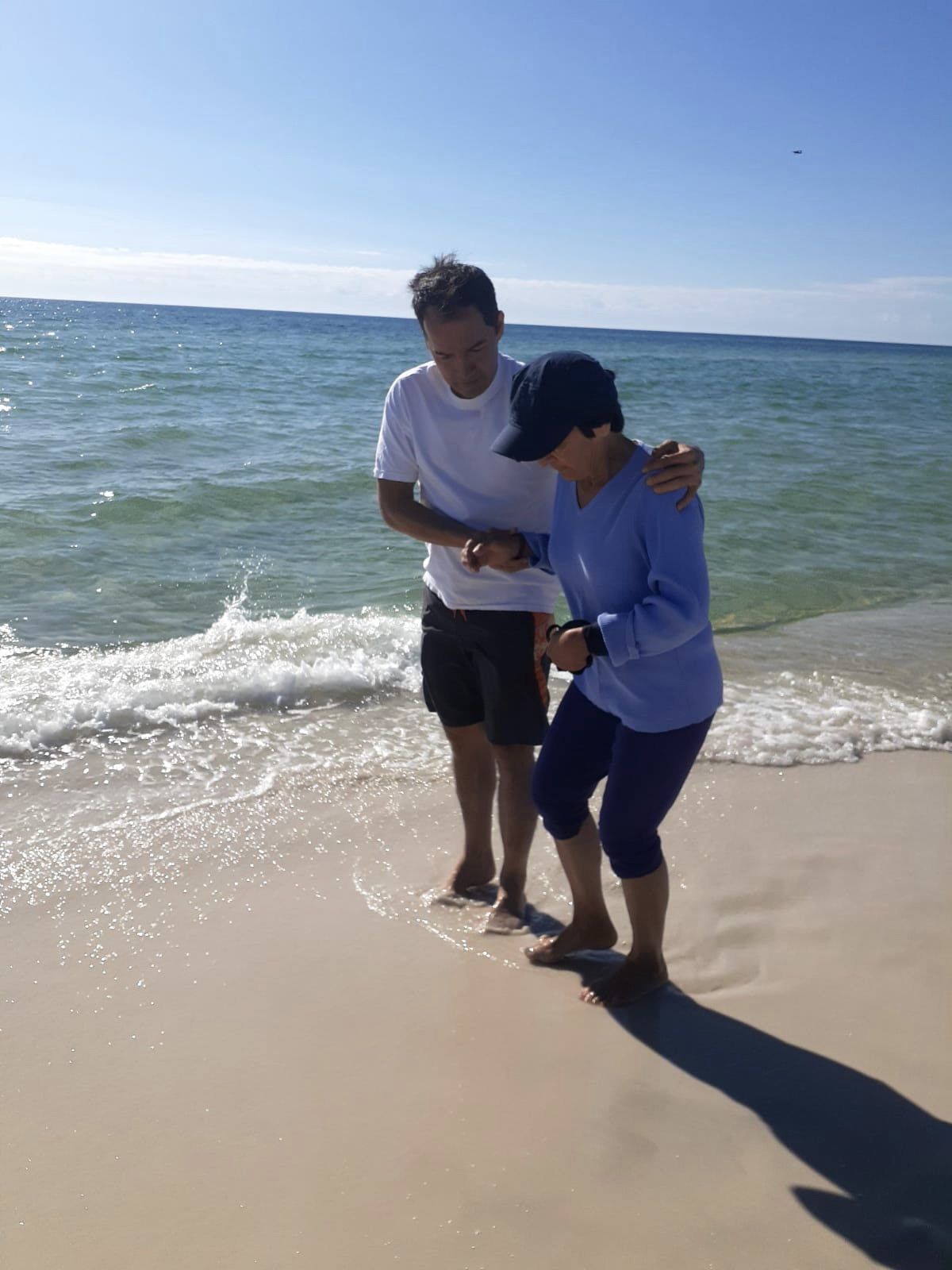 Mary and her son walk on a beach at the edge of the surf together.