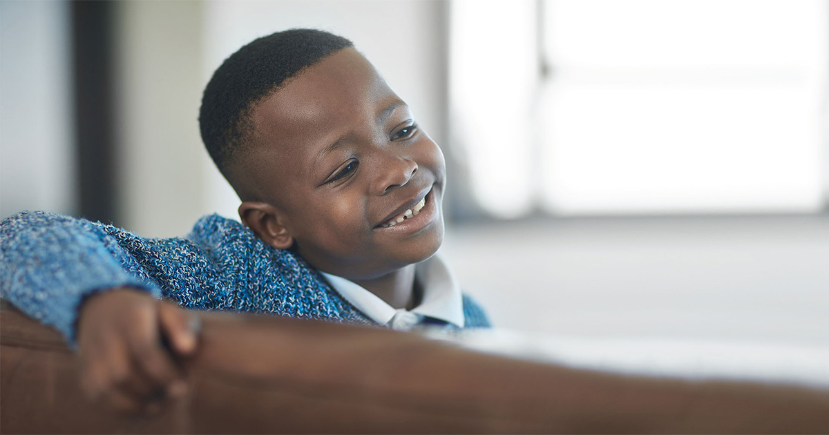 A young boy sitting and smiling on a wooden bench indoors.