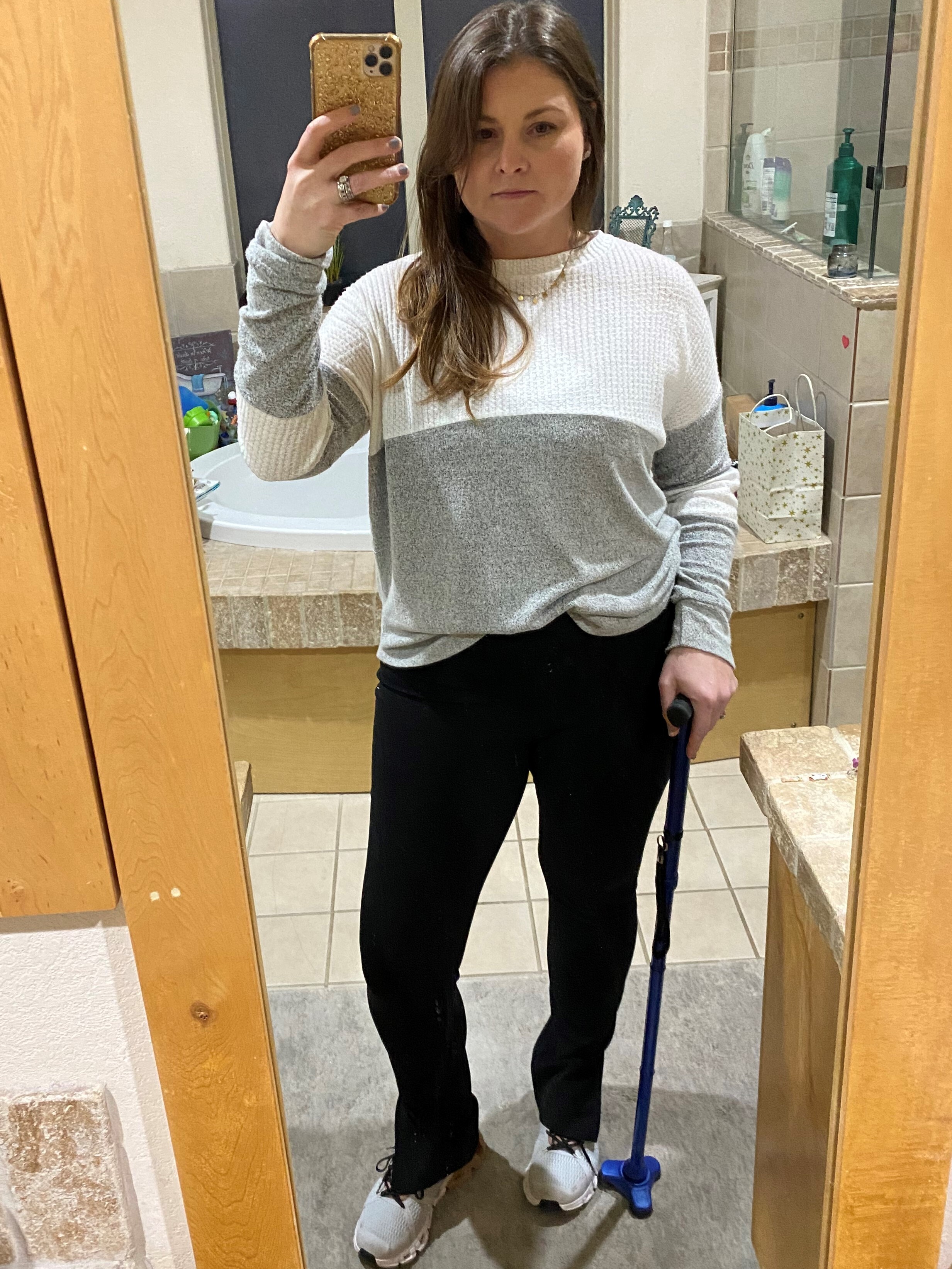 A woman takes a selfie in a mirror and holds a cane with her left hand.