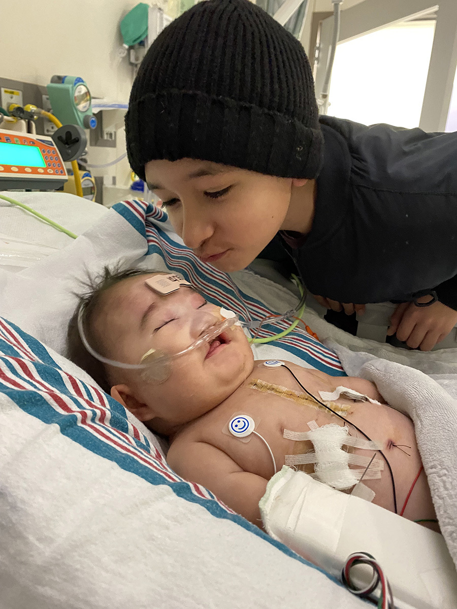 Robert Sedillo, Jr., a young boy wearing a beanie, leaning over to kiss his baby sister Rubi in the hospital