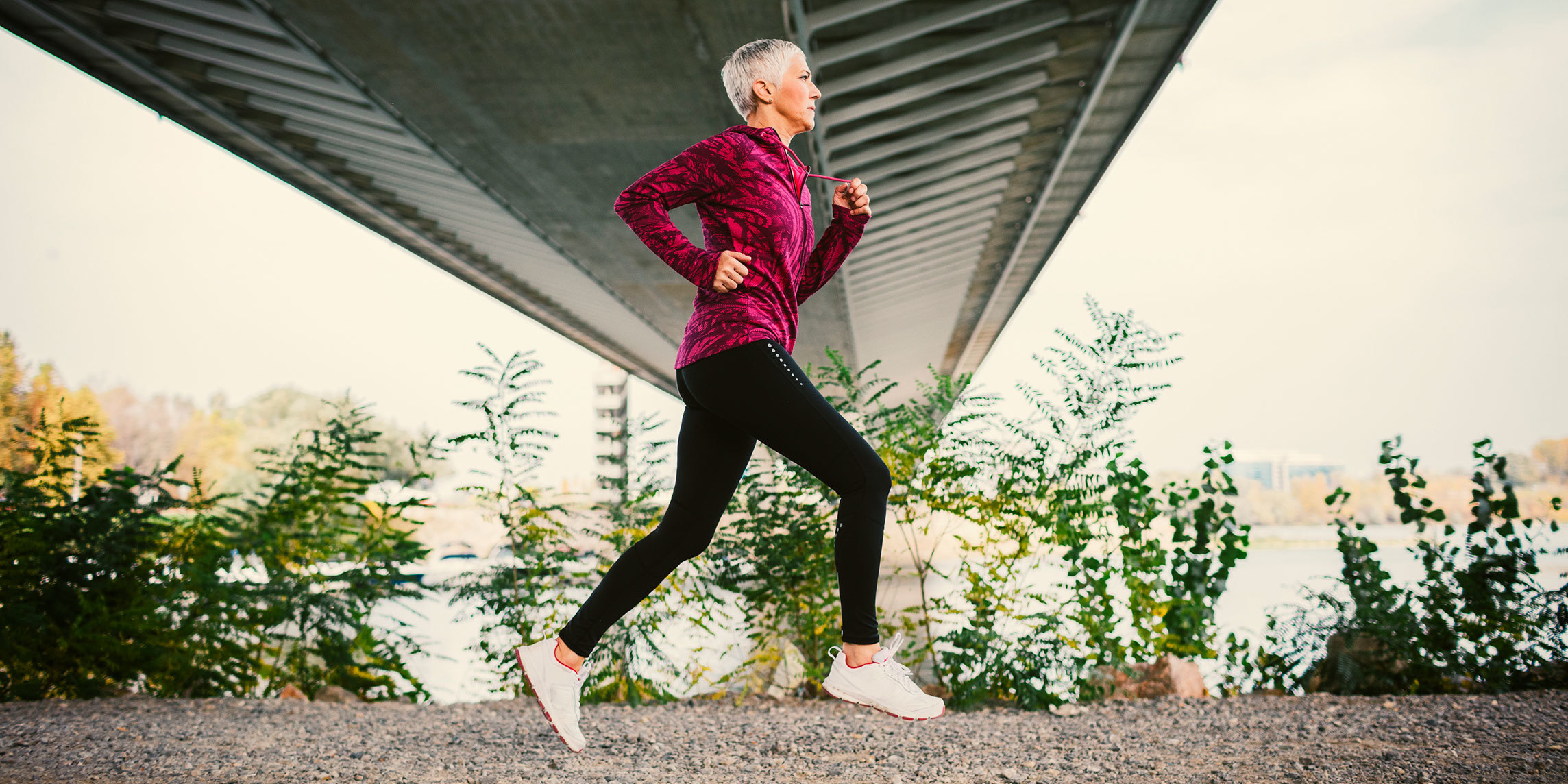 A gray-haired woman jogs under a bridge.