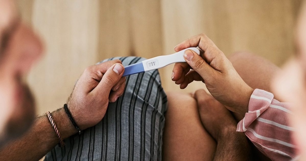 A closeup image of a couple holding a positive pregnancy test in their hands.