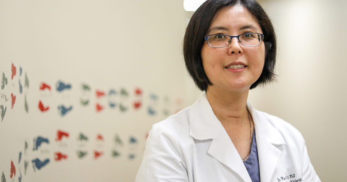 Winifred Mak, MD, PhD, Reproductive Endocrinology and Infertility (REI) Specialist, stands smiling in front of a wall festooned with colorful decorations.