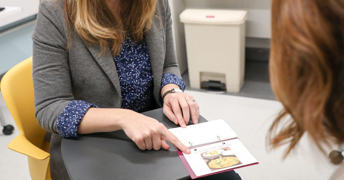 A clinician at UT Health Austin's Comprehensive Memory Center smiles while pointing to a page in a memory book.