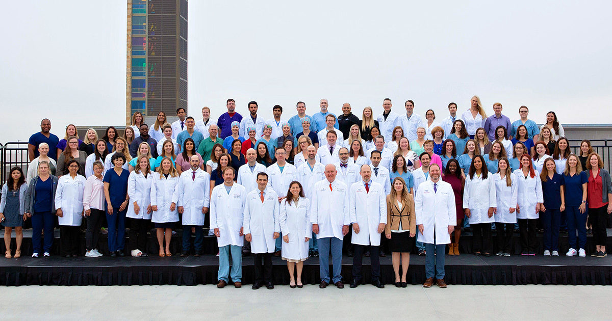 Providers and staff of the Texas Center for Pediatric and Congenital Heart Disease gather on risers for a team photo with the Dell Children's Medical Center tower behind them.