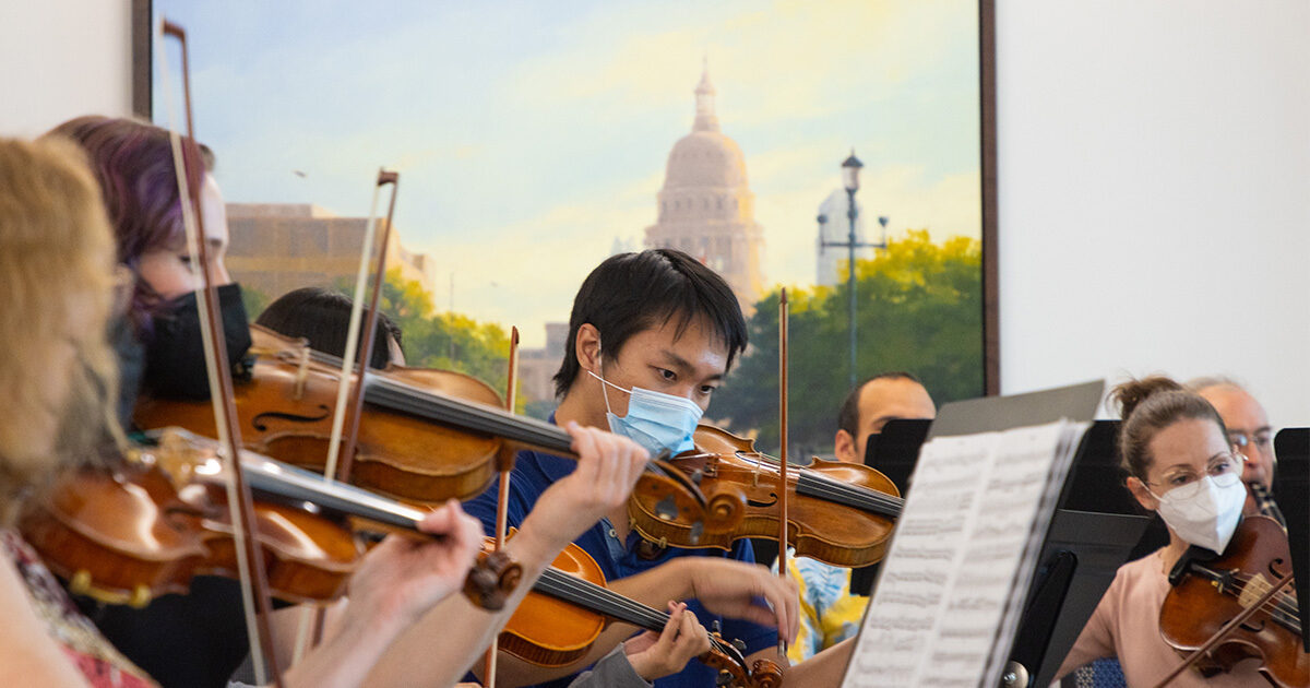 A masked string orchestra performing with the Texas State Capitol building in the background.