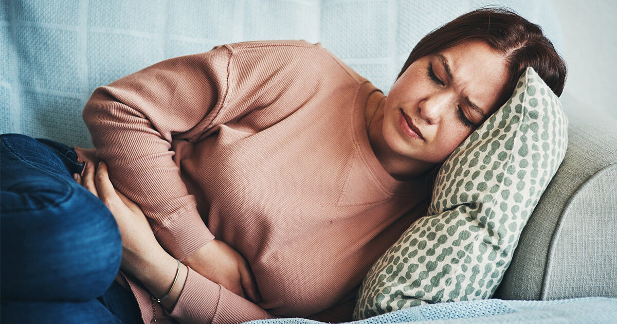 A woman lying on a couch clutches her stomach in discomfort.