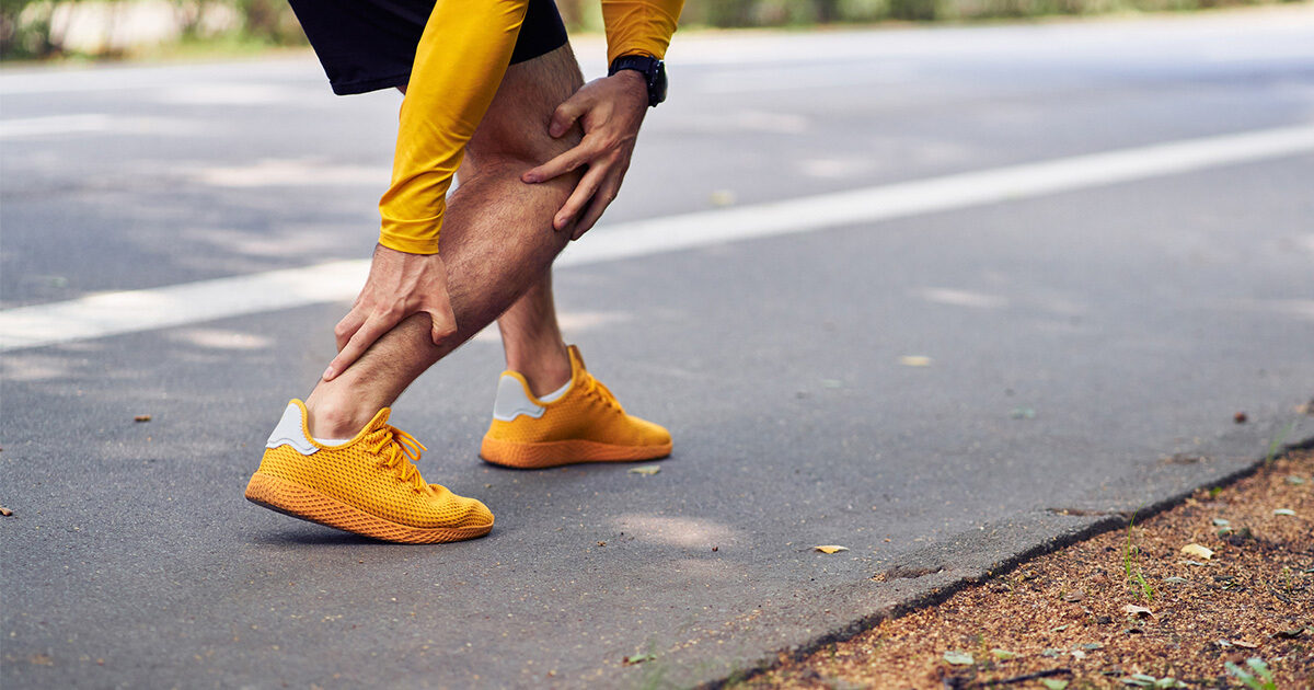 Close-up of a man wearing yellow running shoes grabbing his ankle in discomfort.