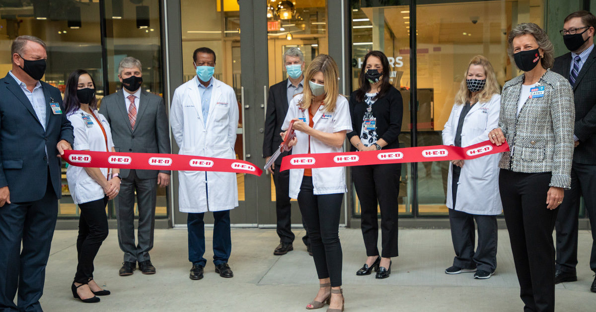 Pharmacists in white coats perform a ribbon cutting to commemorate the opening of the HEB Pharmacy in the Health Transformation Building.