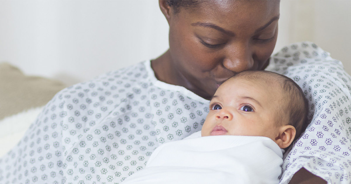 mother wearing hospital gown kissing newborn baby