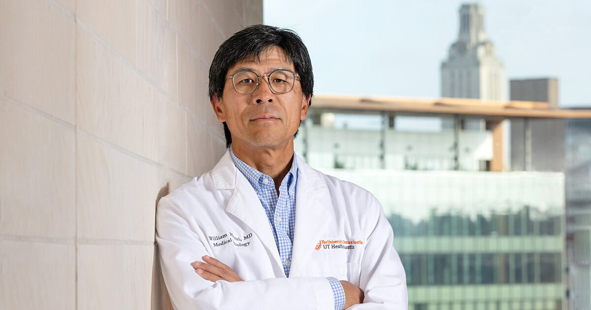 William Matsui, MD, posing in a white lab coat with the UT Tower visible behind him.