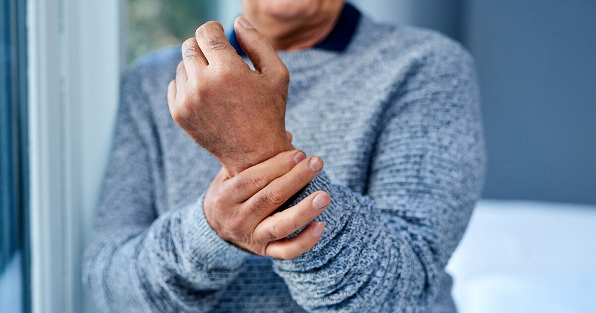 Close-up photo of an older adult holding their wrist in their other hand.