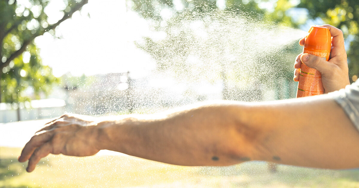 A man spraying insect repellent onto his arm.